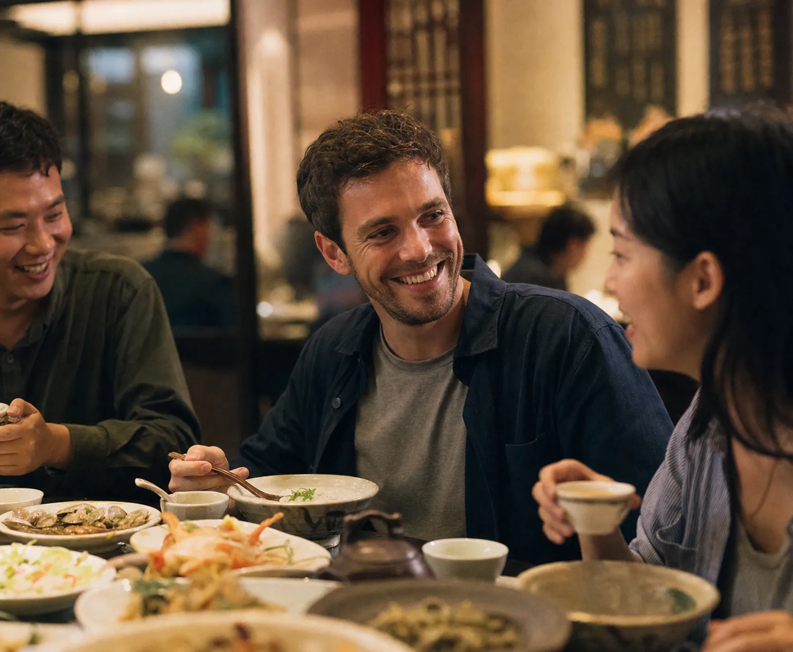 el mismo viajero comparte una comida con amigos en un restaurante de Shantou; cuencos de gachas de arroz, platillos salados, marisco y diminutas tazas de té gongfu en la mesa